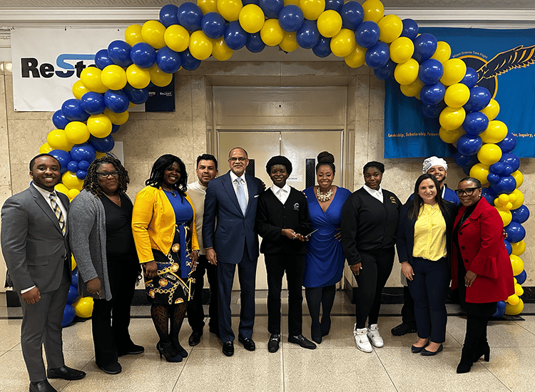 Adults standing under blue and yellow balloon archway