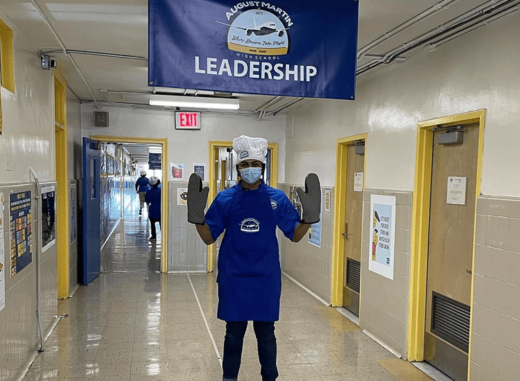 Student standing in the hallway with hands raised wearing oven mitts